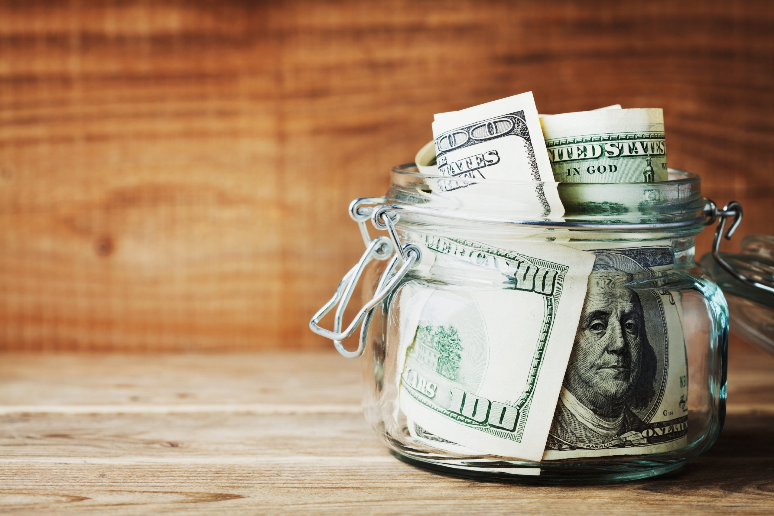 Collections attorney concept. Dollar bills in glass jar on wooden background. Saving money concept.